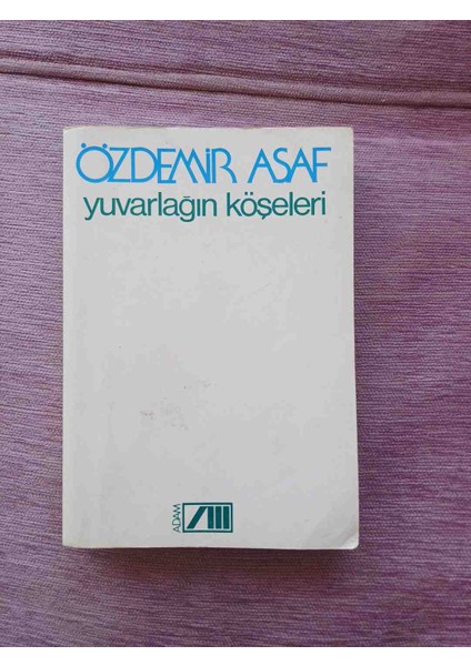Özdemir Asaf'ın 'yuvarlağın Köşeleri' Adlı Romanı, Beyaz Kapak Üzerine Mavi ve Yeşil Yazılı Sade Tasarım Içerir.