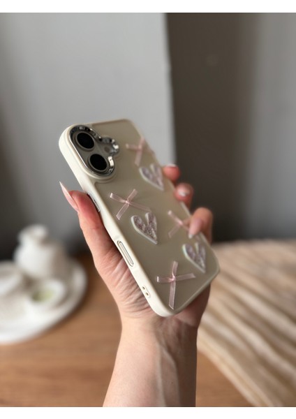 IPHONE 16 3D Kalp ve Fiyonk Dekorlu Ekru Renk Kılıf modelleri